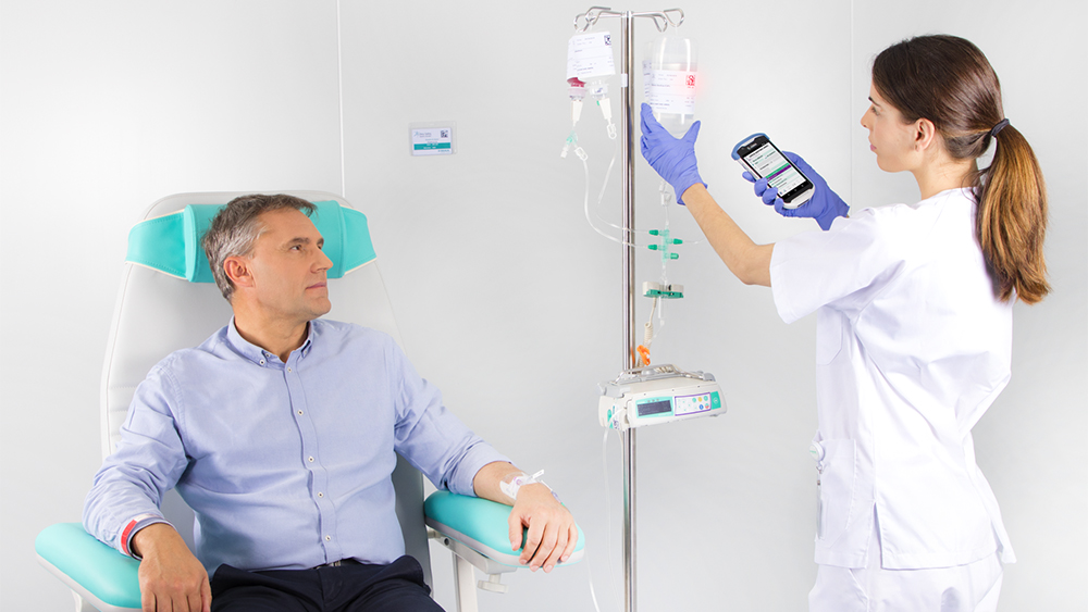 The image shows a patient seated in a chair, receiving an infusion from a B. Braun medical device, while a nurse is seen setting up the infusion dosage on the device.